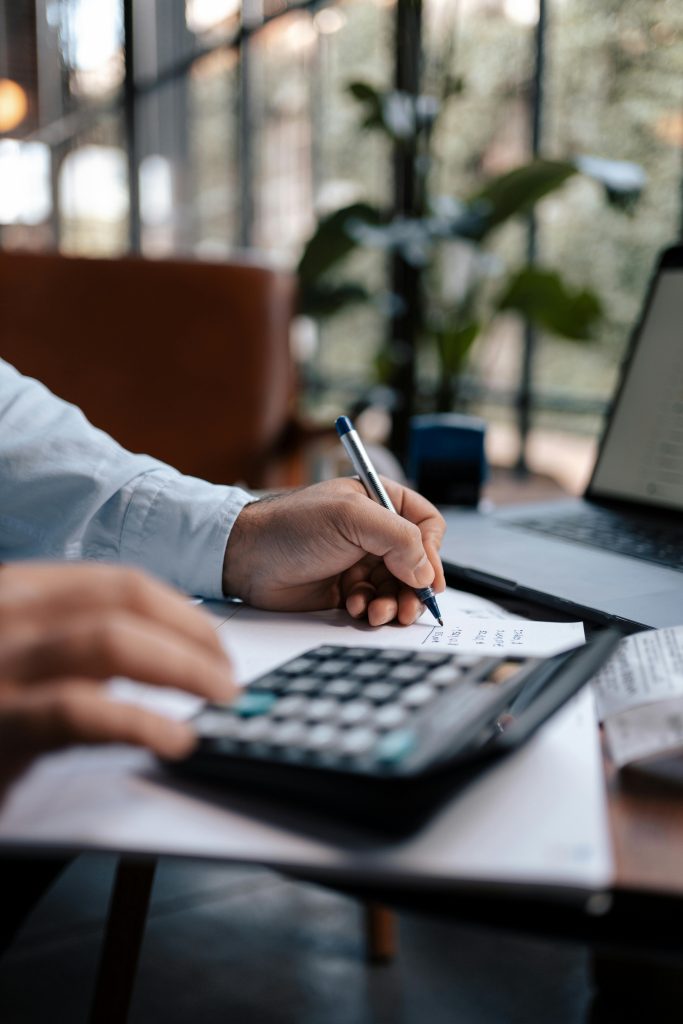 pexels-photo-16282306-16282306 A person calculating finances with a calculator and pen on a desk indoors.