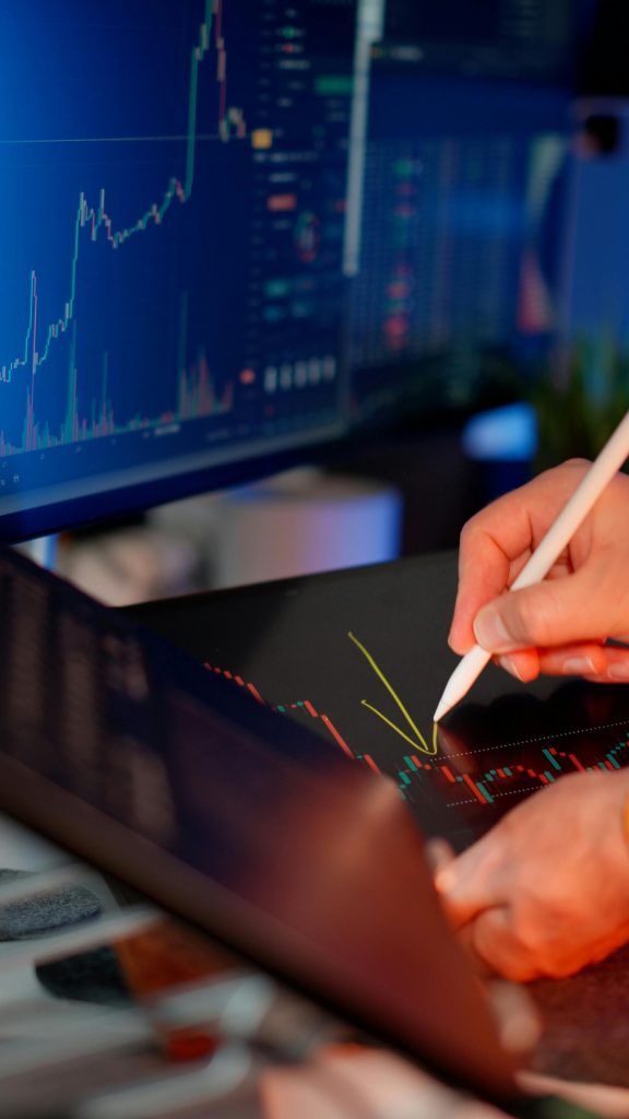 pexels-photo-33000099-33000099 Person using a stylus on a tablet for stock market analysis, with charts on a monitor.