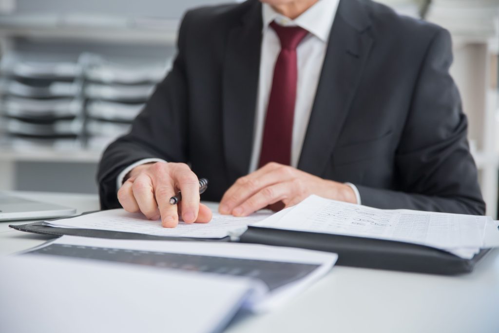 pexels-photo-8428064-8428064 Close-up of a businessman reviewing documents at an office desk. Focus on hands and paperwork.